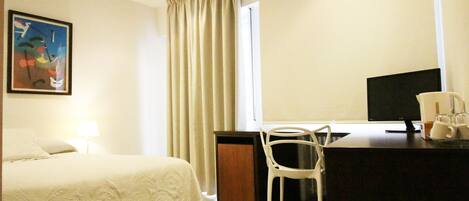 A hotel room with a bed, a desk with a chair, a television, and a window with curtains.