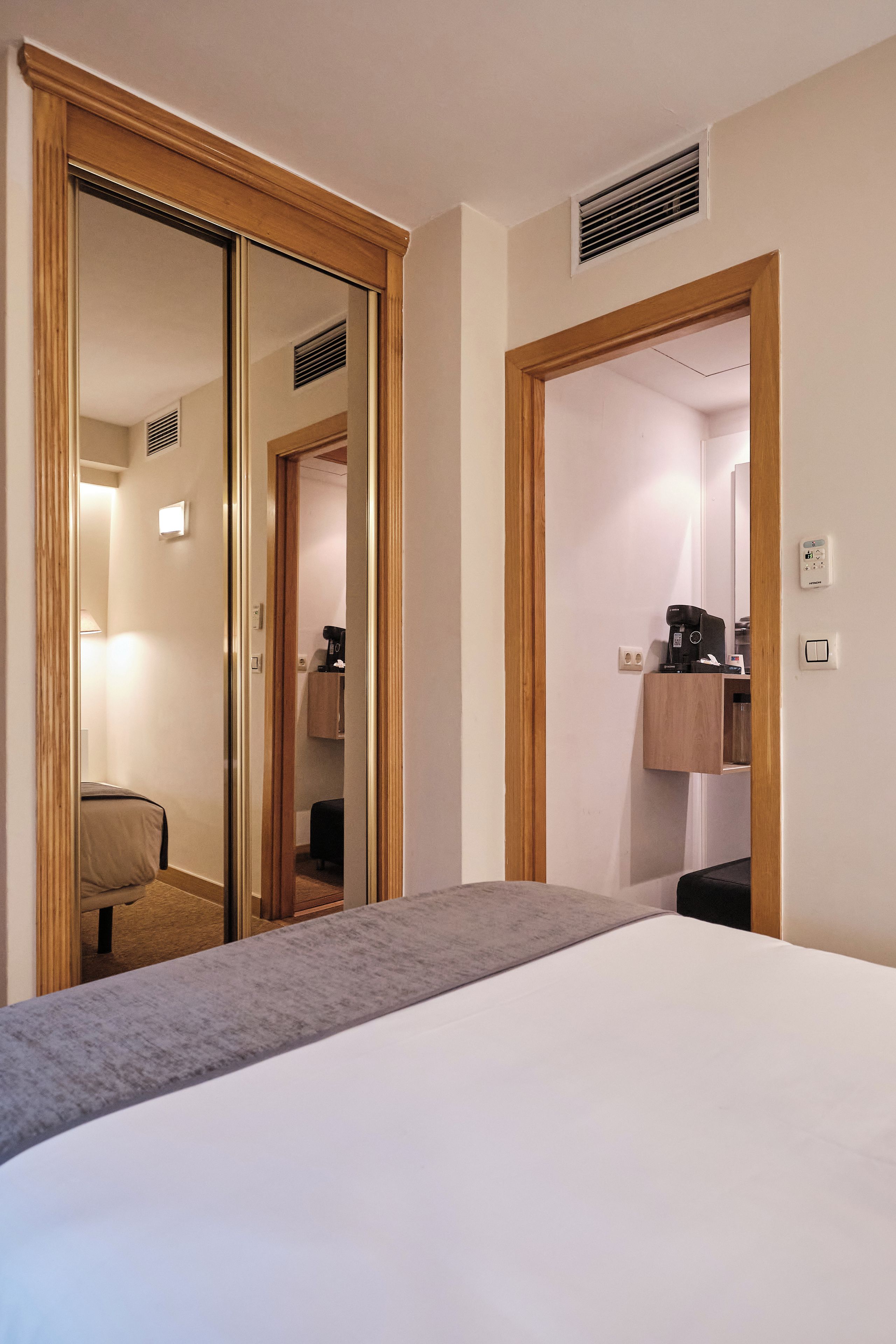 Habitación de hotel con una cama grande, un espejo, un armario y un baño visible a través de una puerta abierta.