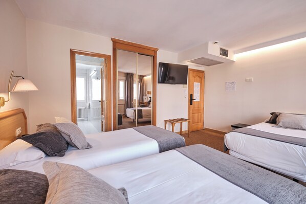 Habitación de hotel con dos camas, televisor, espejo y baño visible a través de una puerta abierta.