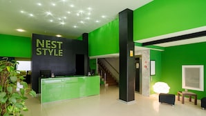 A reception area with a green reception desk, a staircase, and a wall with 'NEST STYLE' signage. - Nest Style Santiago (Santiago de Compostela)