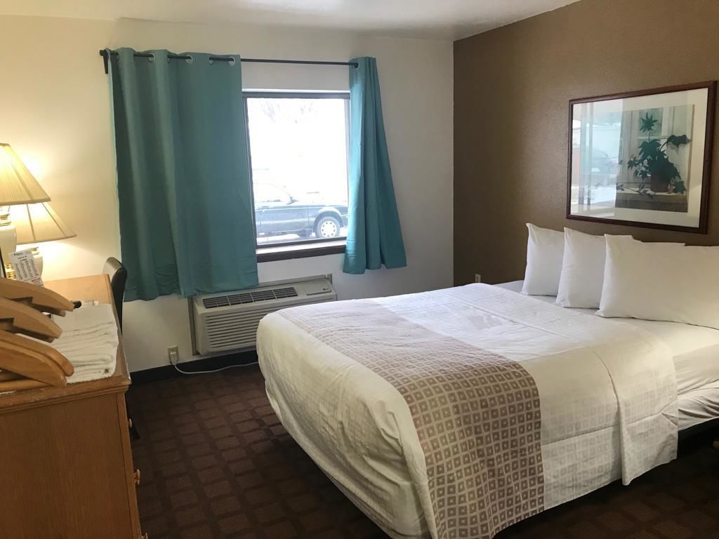 A hotel room with a bed, a window with curtains, a heater, and a framed picture on the wall.