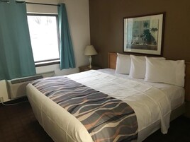Una habitación de hotel con una cama, un ventanal con cortinas, una lámpara de pared y un cuadro enmarcado.