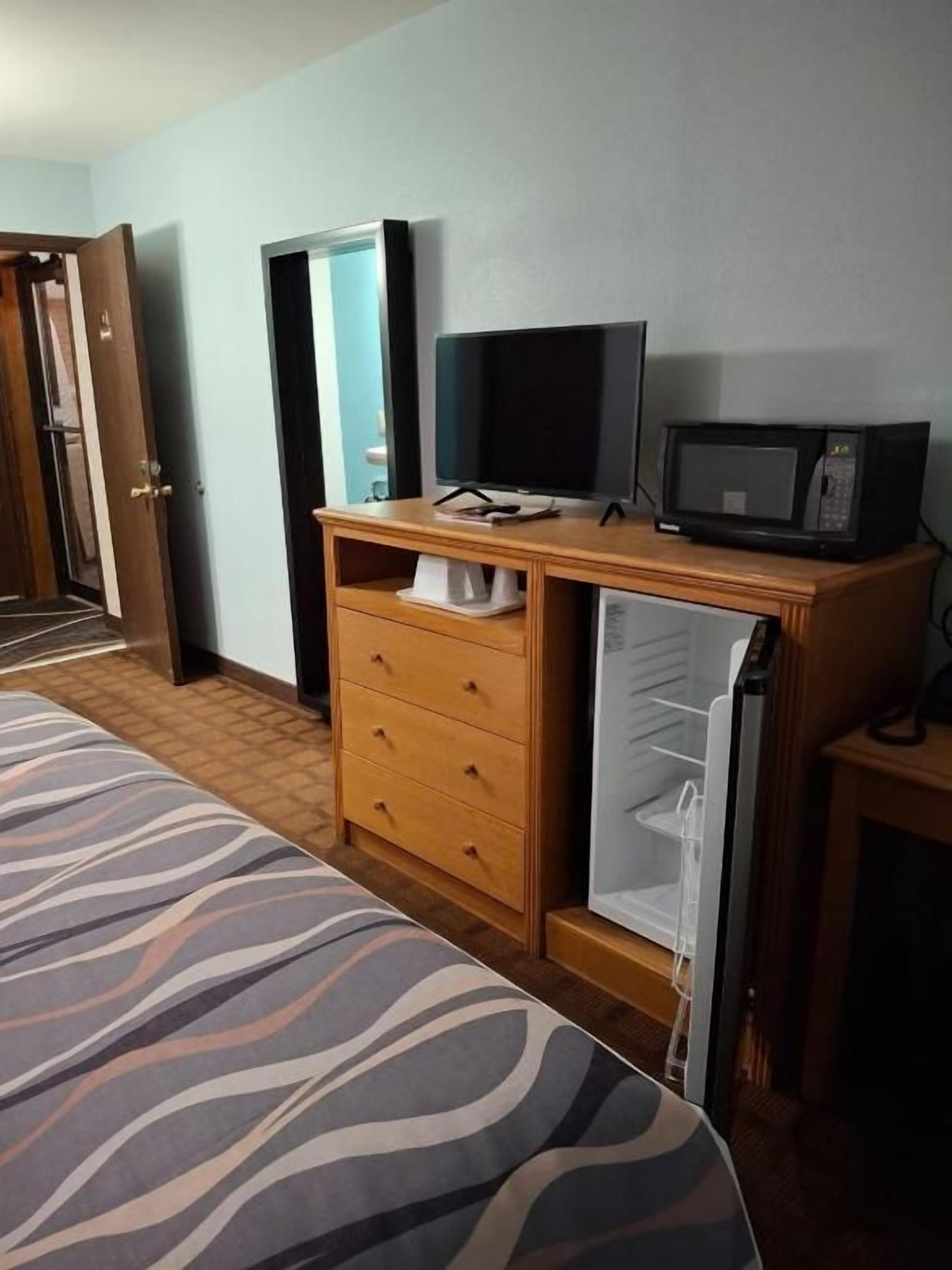 Ein Hotelzimmer mit einem Bett, einer Holzkombination, einem Fernseher, einer Mikrowelle und einer Tür zu einem weiteren Raum.