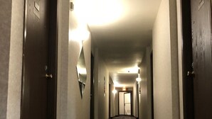 Un couloir d’hôtel avec un sol recouvert de moquette, des portes des deux côtés et un luminaire fixé au mur.