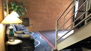 A hotel lobby with a brick wall, a sofa with cushions, a lamp, a carpet with wavy lines, and an exit sign. - Valued Stay Sun Prairie (Sun Prairie)