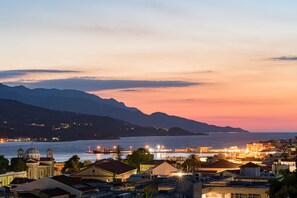 A coastal town at dusk with a prominent church, waterfront buildings, and a mountainous backdrop.