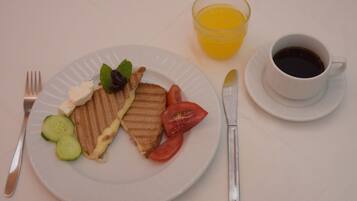 Een bord met een gegrilde kaas sandwich, tomaat, komkommer en een kleine salade. Op tafel staat een glas sinaasappelsap en een kop zwarte koffie.