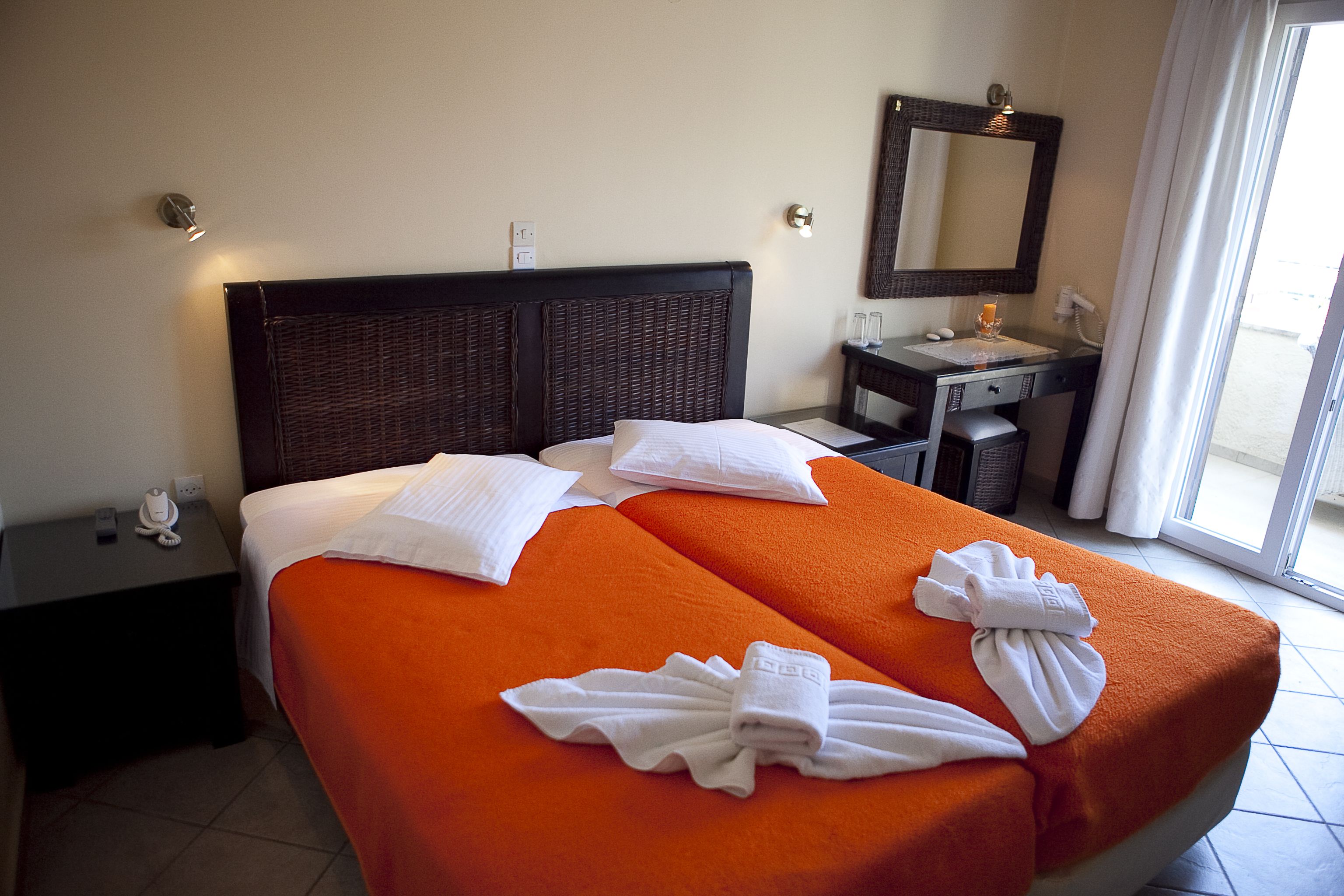 A hotel room with two beds, a desk, a mirror, and a window with curtains.