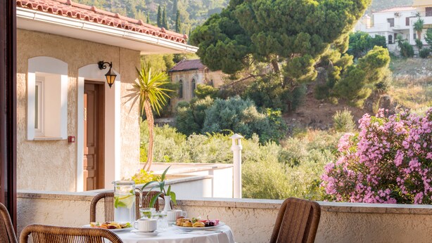 A terrace with a table set for dining, overlooking a hillside with trees and a building.