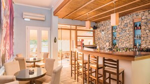 A bar area with wooden chairs and a glass table, a stone wall with shelves of bottles, and a large window with a view.