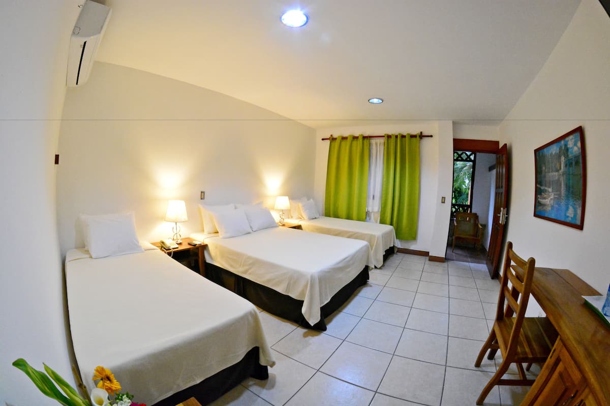 A hotel room with three single beds, a wooden dining table, and a green curtain.