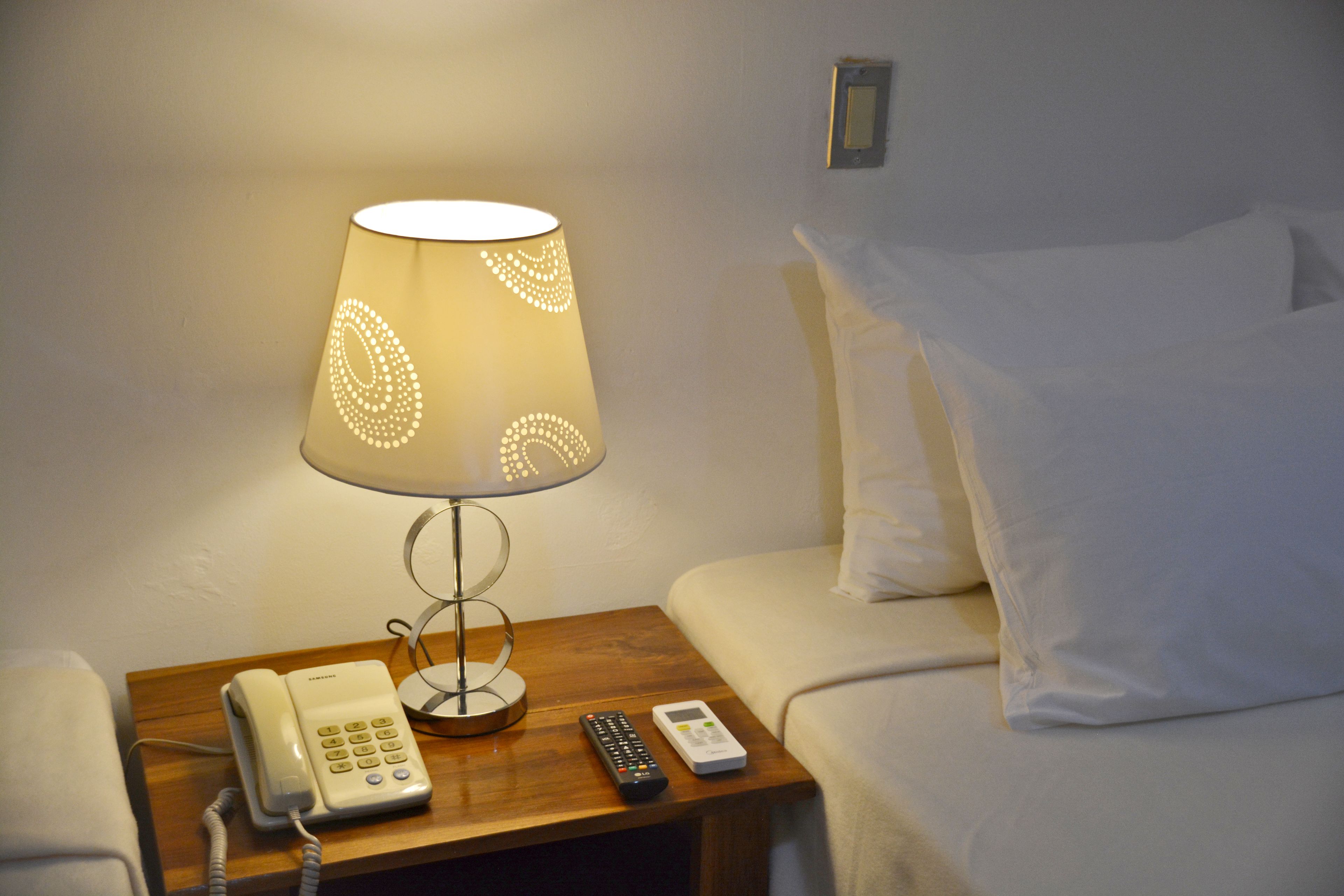 A bedside table with a lamp, a telephone, and a remote control.