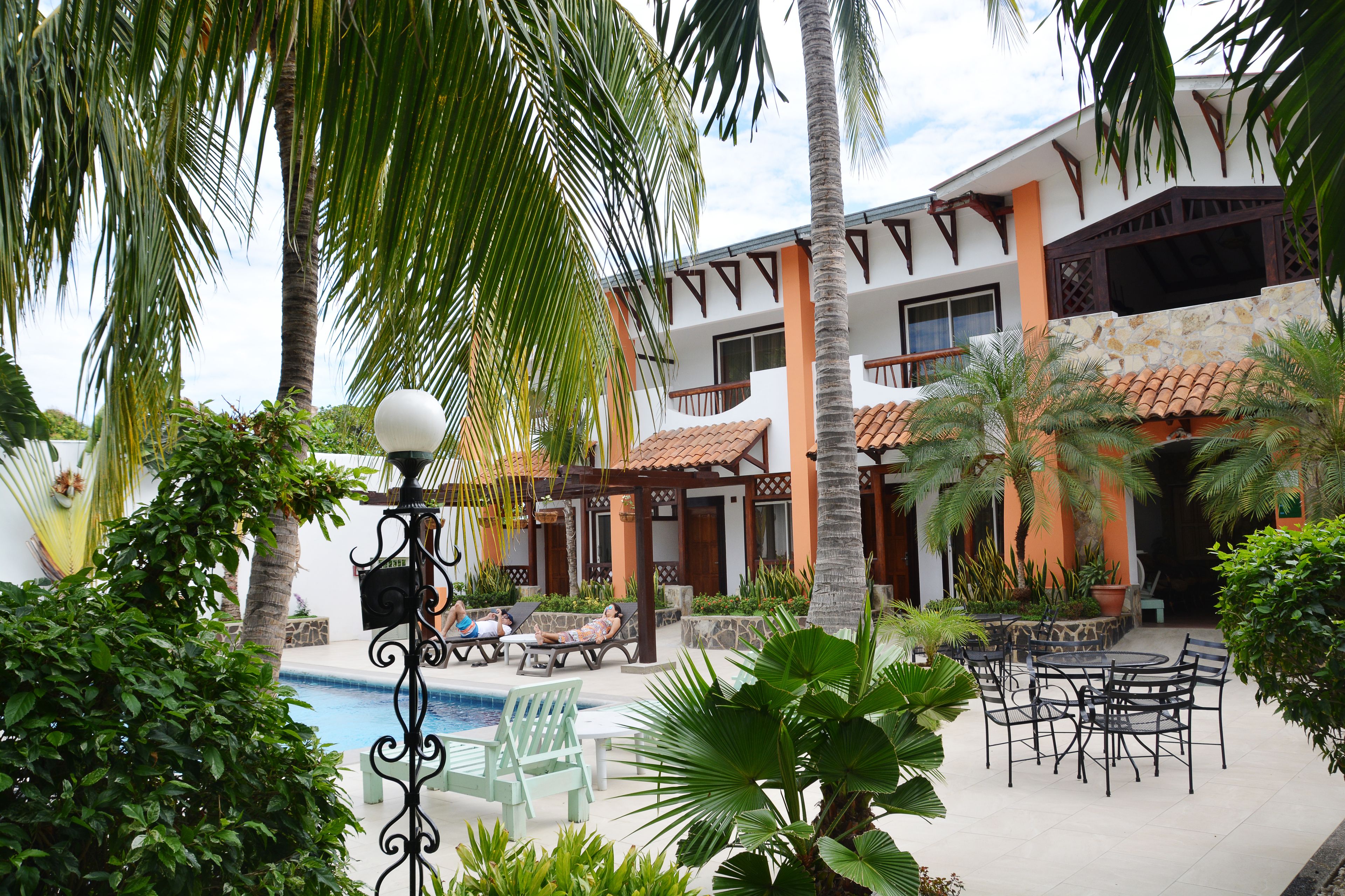 A pool area with lounge chairs and a dining table, surrounded by palm trees and potted plants.