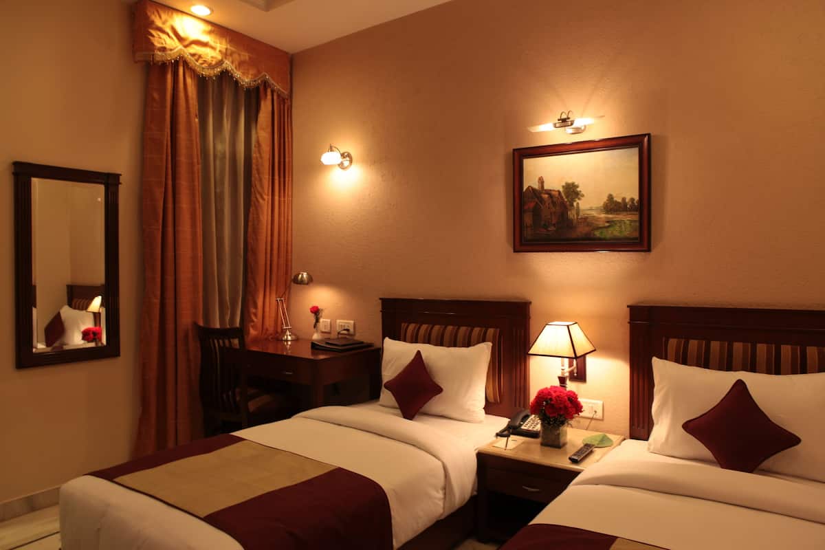 A hotel room with two beds, a nightstand with a lamp, a telephone, and a painting on the wall.