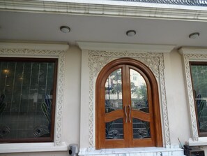 Fachada de edificio con un gran arco de madera, molduras decorativas y una ventana con tejas formando un patrón de cuadrícula.