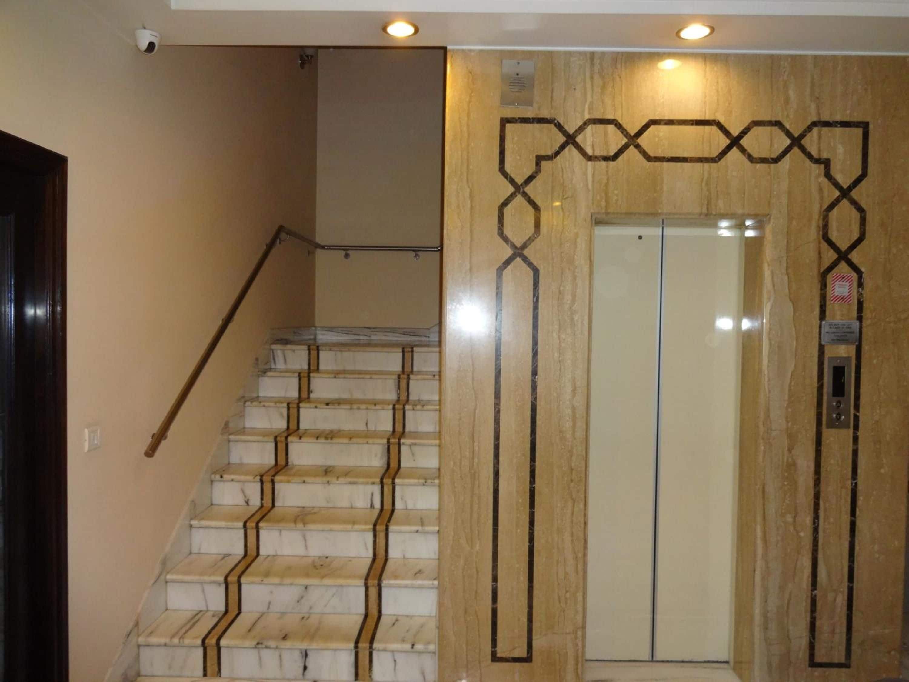 A staircase with marble steps and a handrail, leading to an elevator with a geometric wall design.