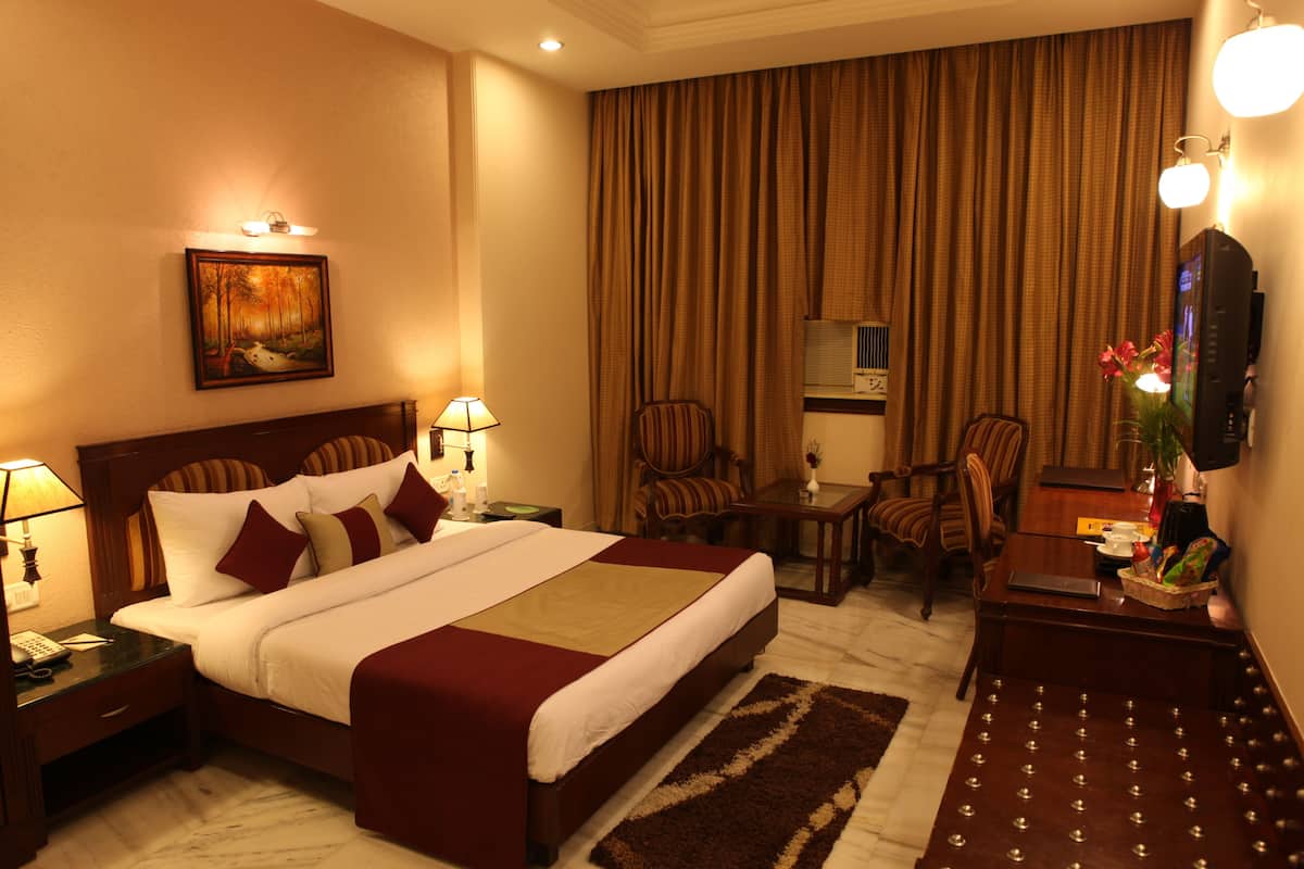 A hotel room with a large bed, a desk, two chairs, a television, and a painting on the wall.