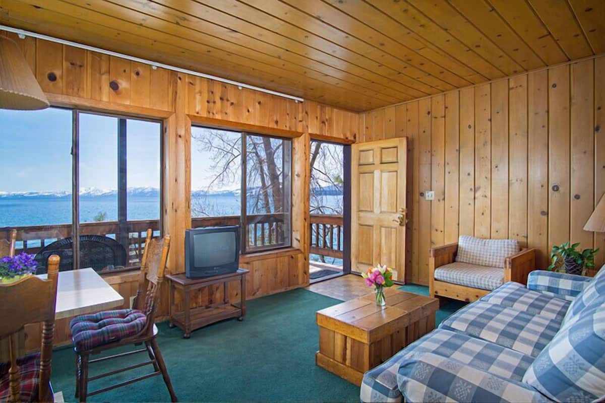 Une cabane avec un intérieur en bois, une télévision, un canapé et une table ornée d’un vase de fleurs.