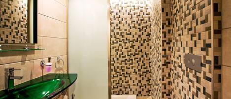 Un baño moderno con lavamanos de vidrio, inodoro y zona de ducha.