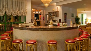 A bar area with a marble counter, red cushioned stools, a chandelier, and a wine bottle display. - Alexandra Beach Hotel (Kos)