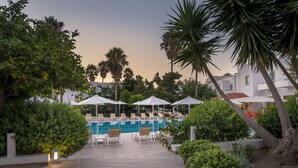 A poolside area with lounge chairs and umbrellas, surrounded by greenery and palm trees. - Alexandra Beach Hotel (Kos)