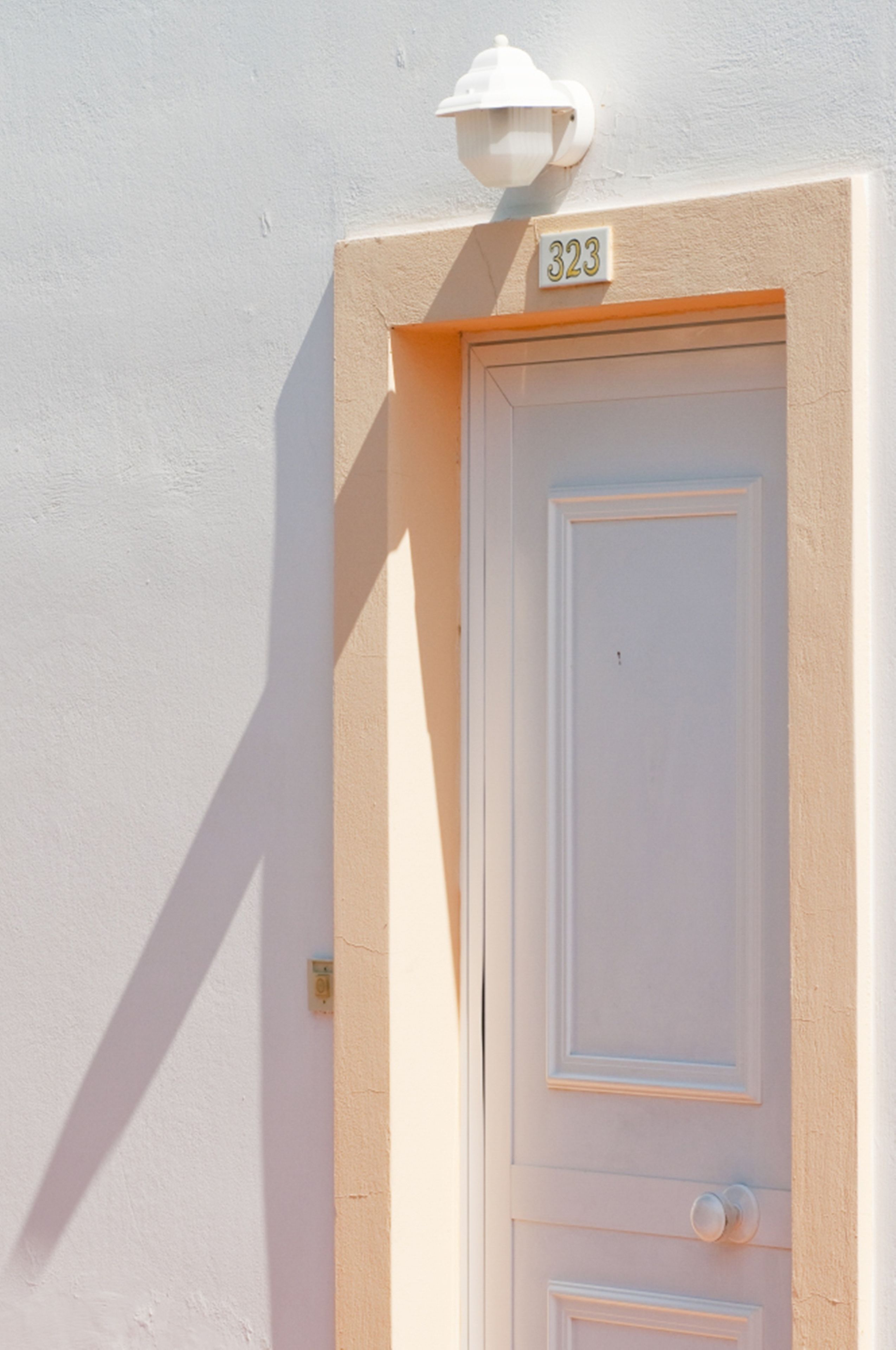 A white door with a number plate '323' and a wall-mounted light fixture above it.