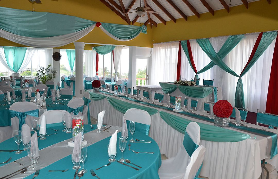 A banquet hall with tables set for a formal event, draped with teal and white fabric, and featuring a ceiling fan.
