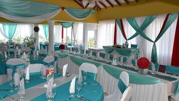 A banquet hall with tables set for a formal event, draped with teal and white fabric, and featuring a ceiling fan.