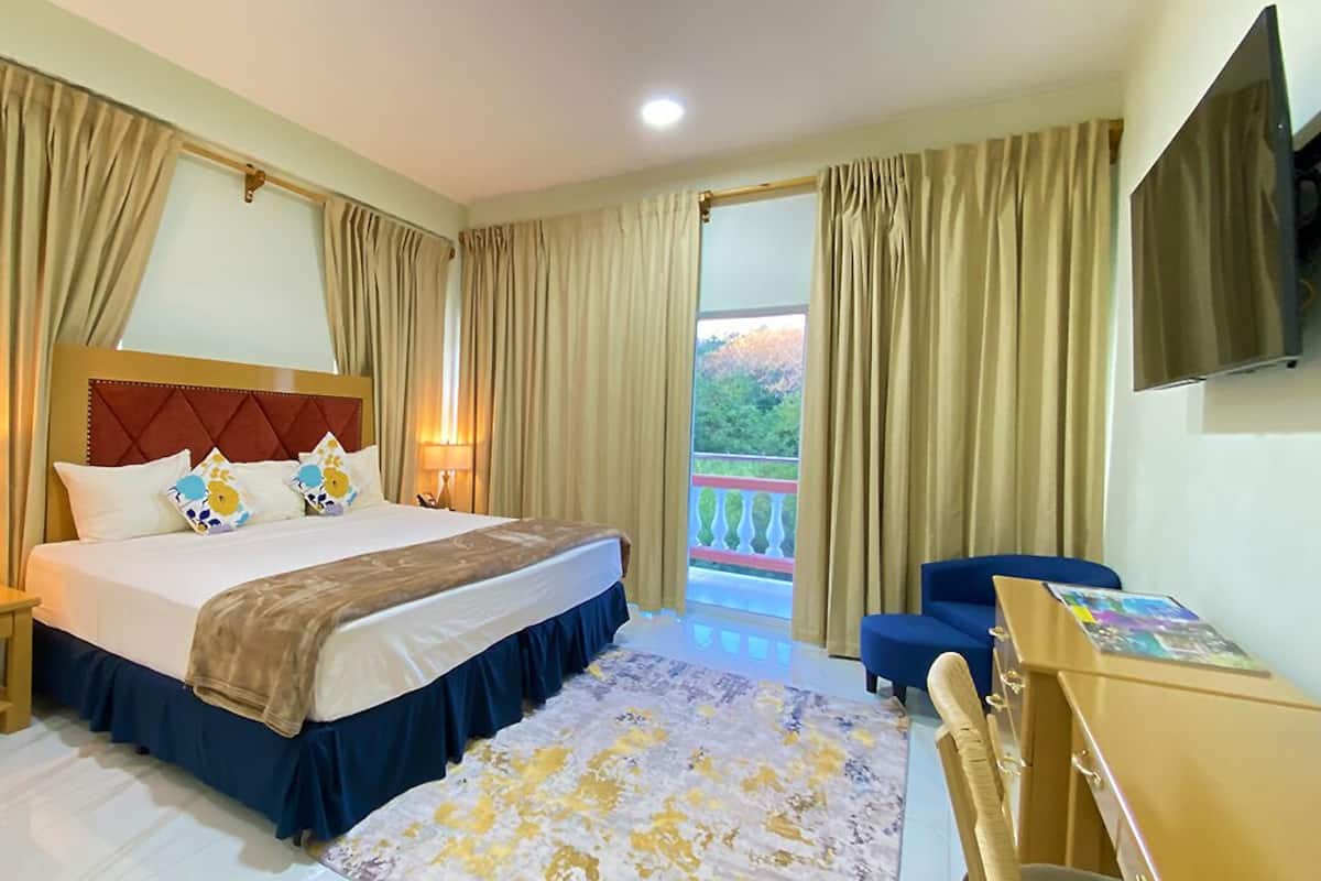 Ein Hotelzimmer mit Bett, Nachttischen, Schreibtisch, Stuhl und einem Balkon mit Vorhängen.