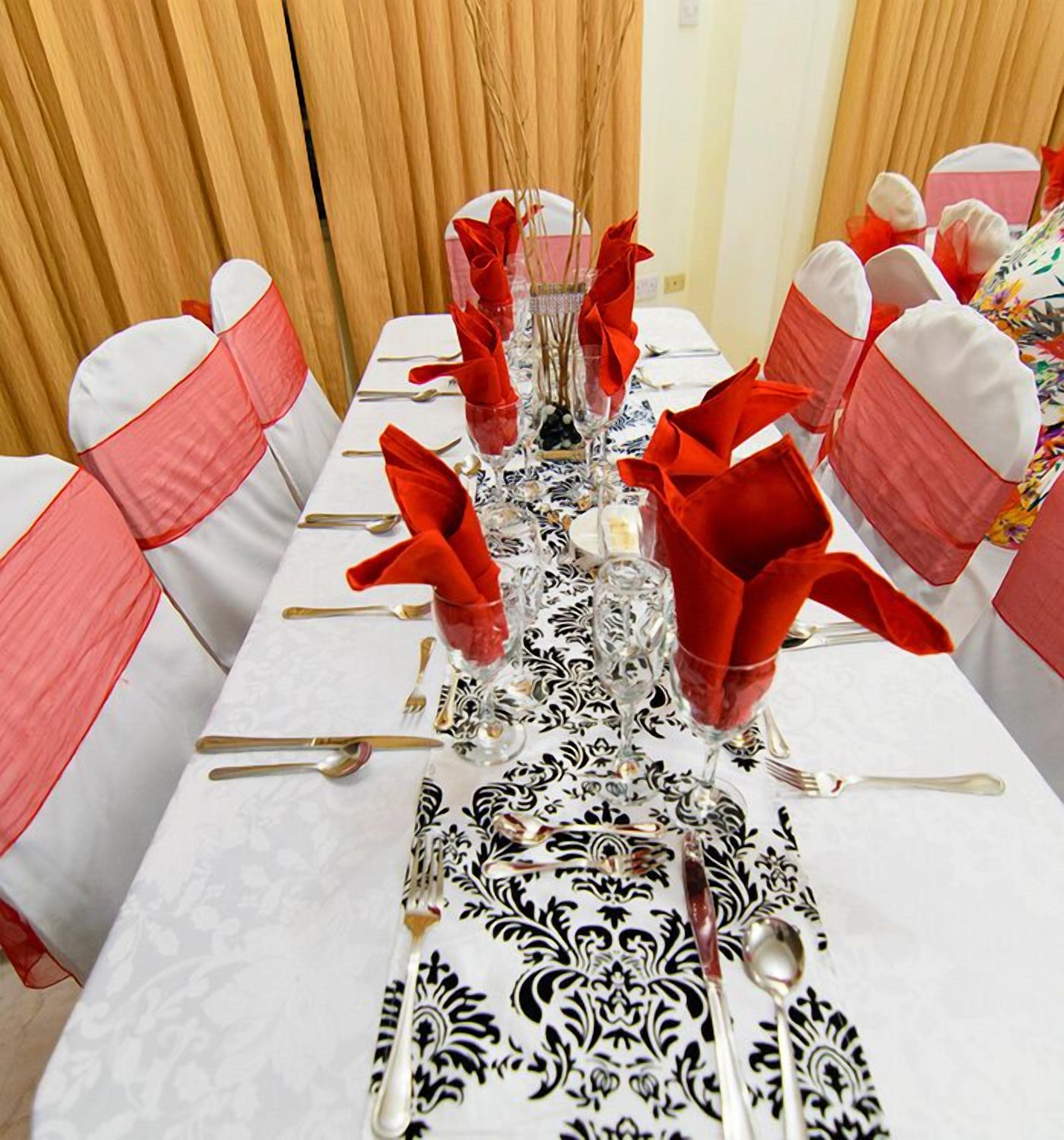 A dining table set with red napkins, white tablecloth, and black and white patterned table runner.