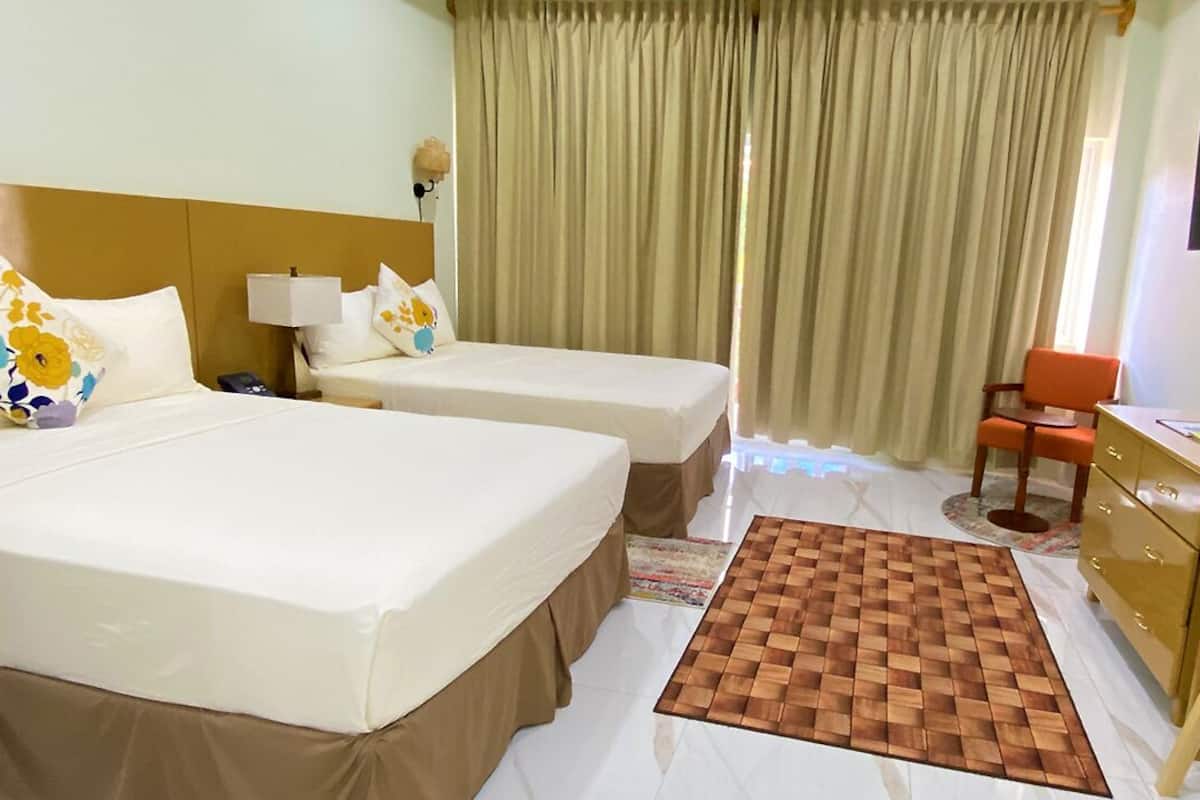 Ein Hotelzimmer mit zwei Betten, einem Schreibtisch, einem Stuhl, einer Uhr und Vorhängen.