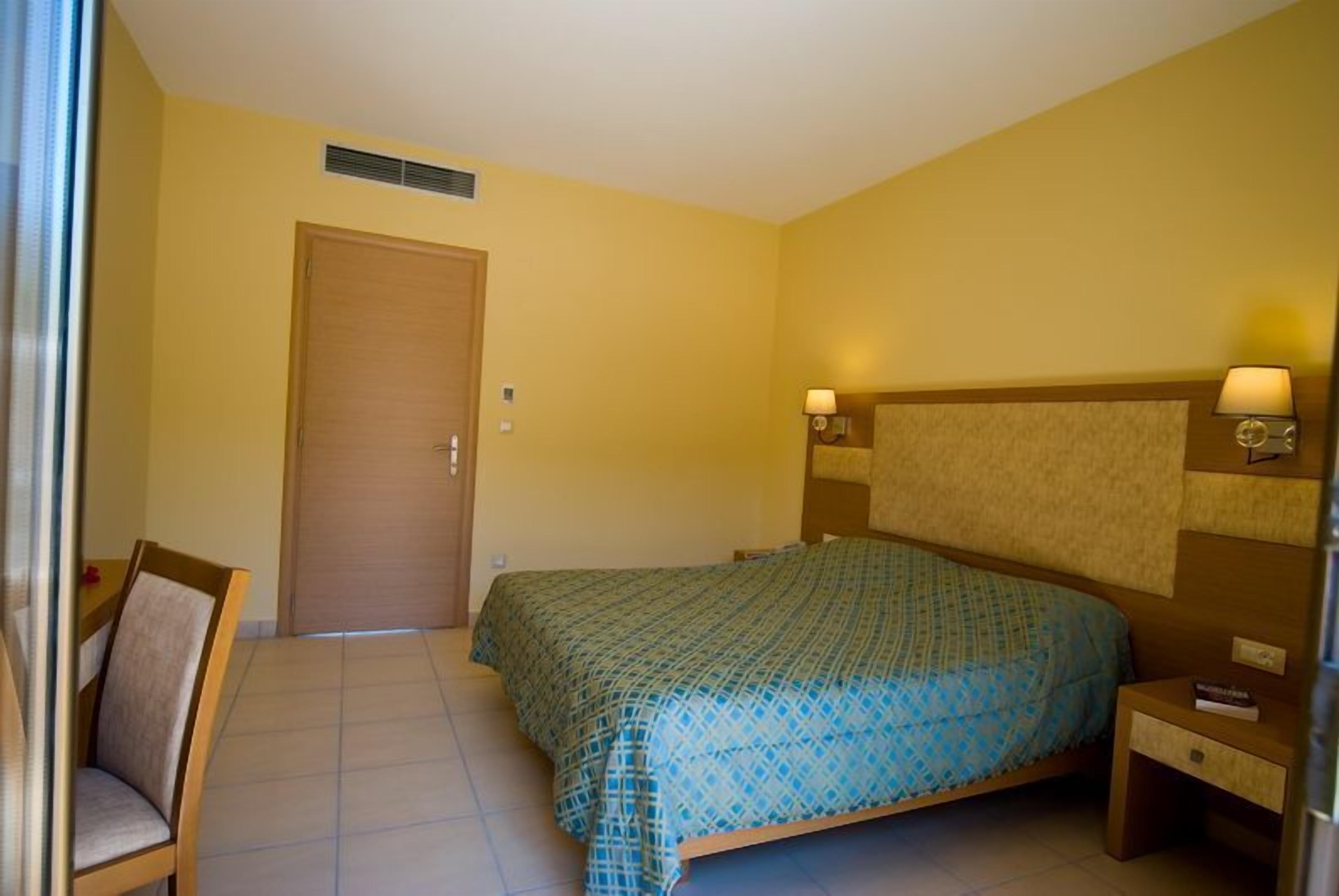 A hotel room with a bed, a chair, a nightstand, and a door.