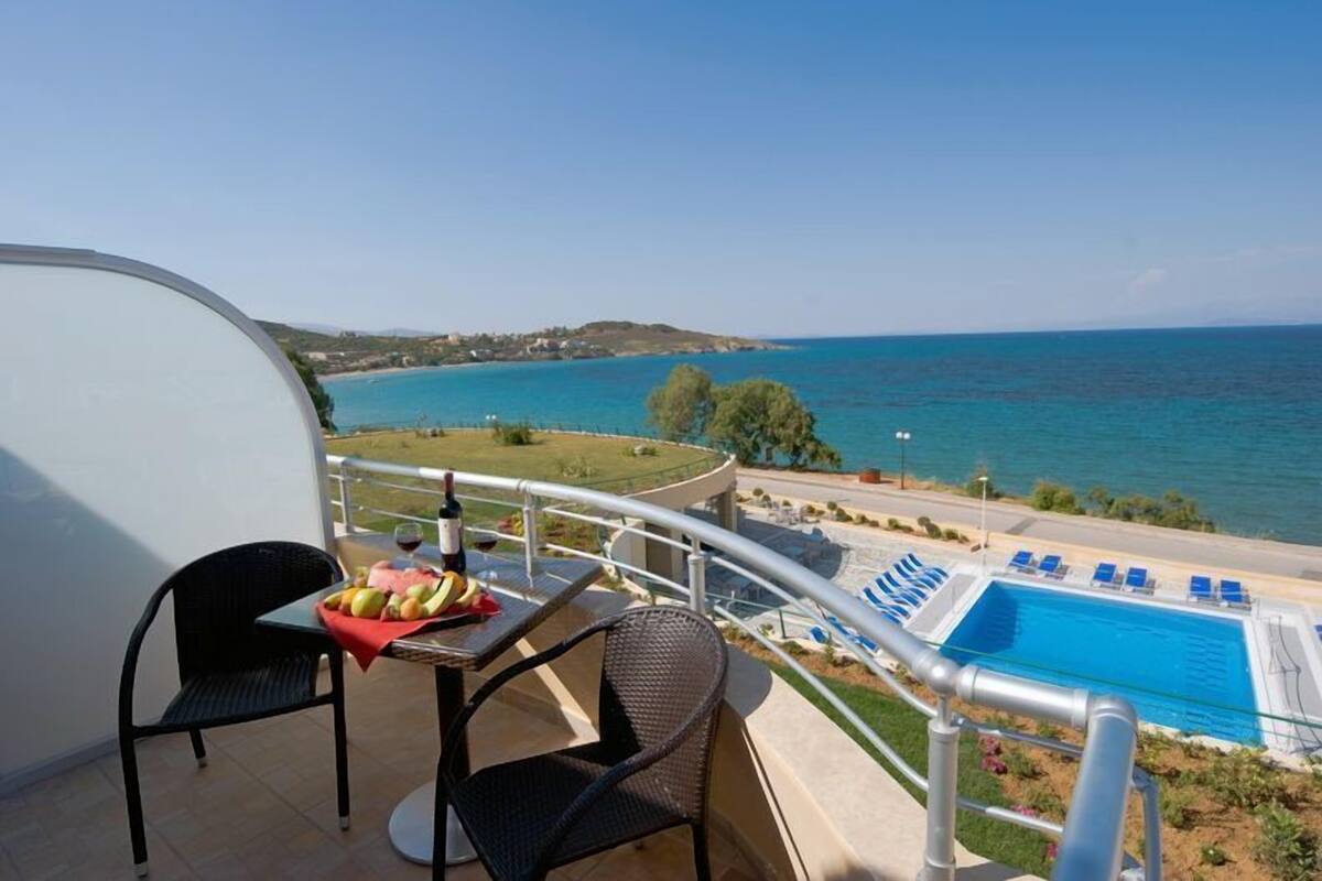 Un balcon avec une table et des chaises, donnant sur une piscine et offrant une vue sur la côte.