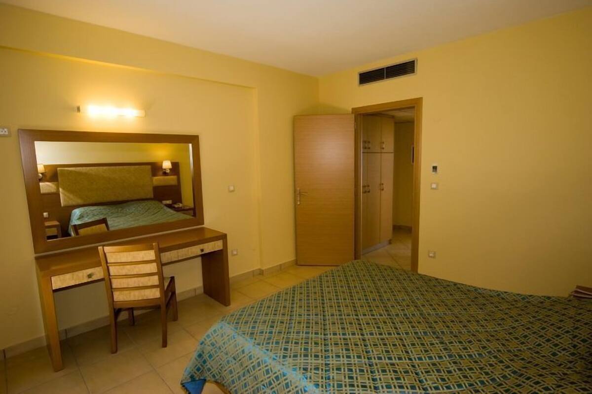 Une chambre à coucher comprenant un lit, un bureau, une chaise, une armoire et un miroir.
