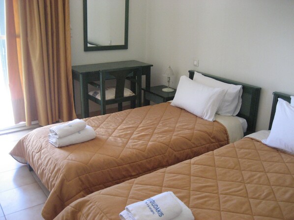 Habitación de hotel con dos camas, cada una con una colcha marrón acolchada y almohadas blancas. Entre las camas, una mesita de noche de madera con una lámpara.