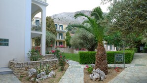 A courtyard with stone pathways, a palm tree, and a building with balconies. - Kyveli Apartments (Chios)