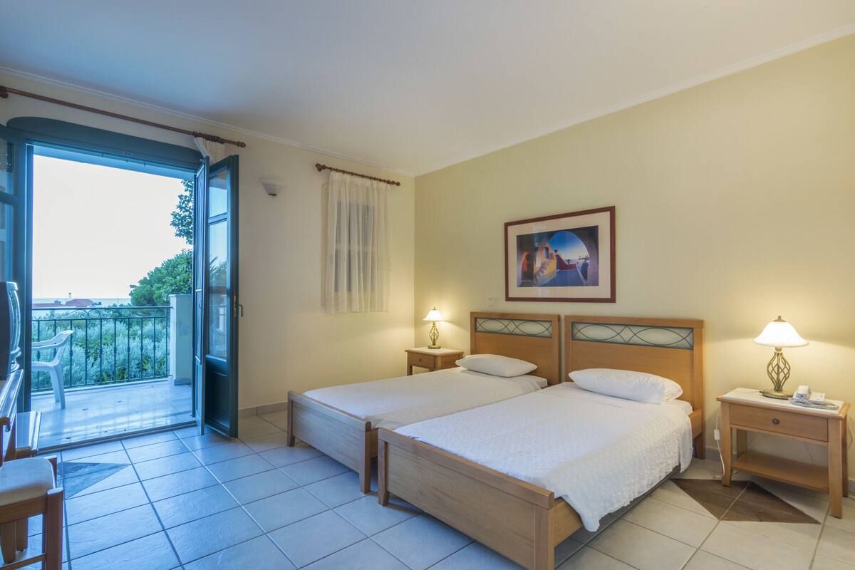 A hotel room with two beds, a balcony with a chair, and a painting on the wall.