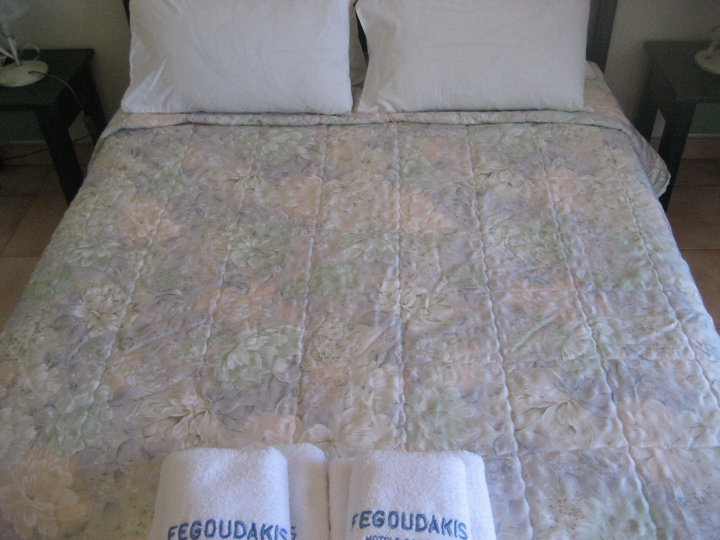 A bed with a floral-patterned bedspread and two towels with 'FEGOUDAKIS' text.