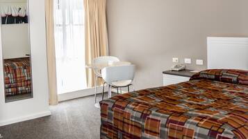 A hotel room with a bed, a desk with a telephone, a chair, and a window with curtains.