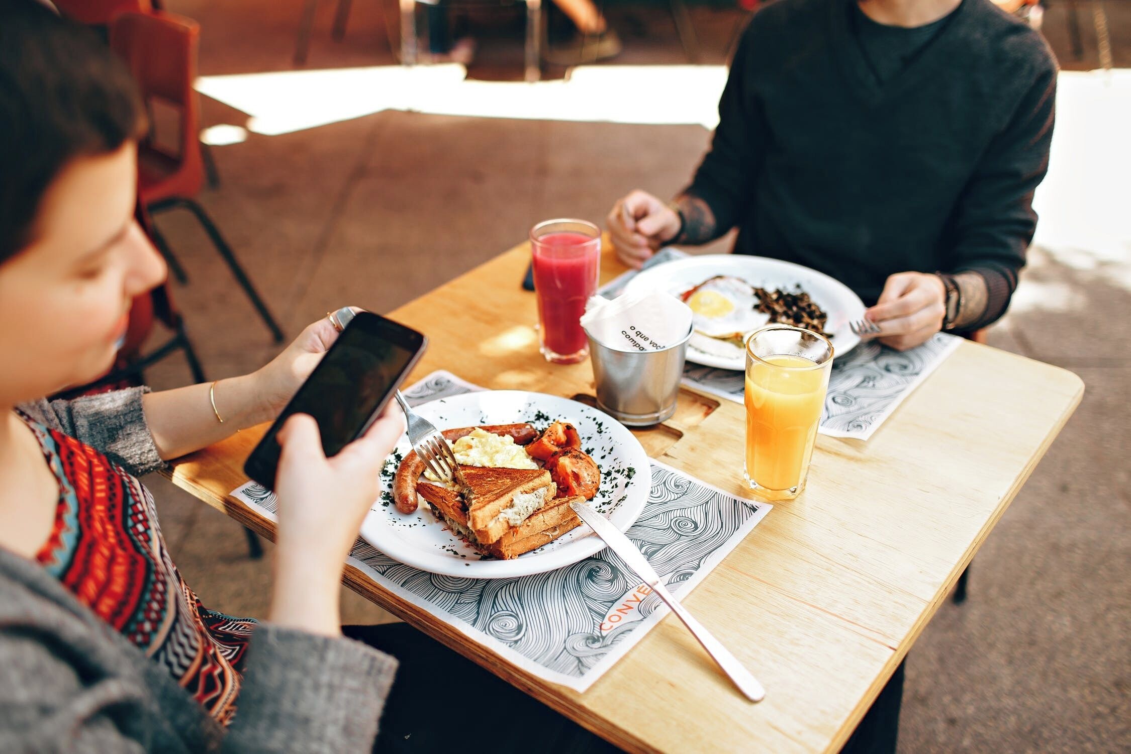 Une table en bois avec des assiettes de petit-déjeuner, un téléphone intelligent et une boisson.