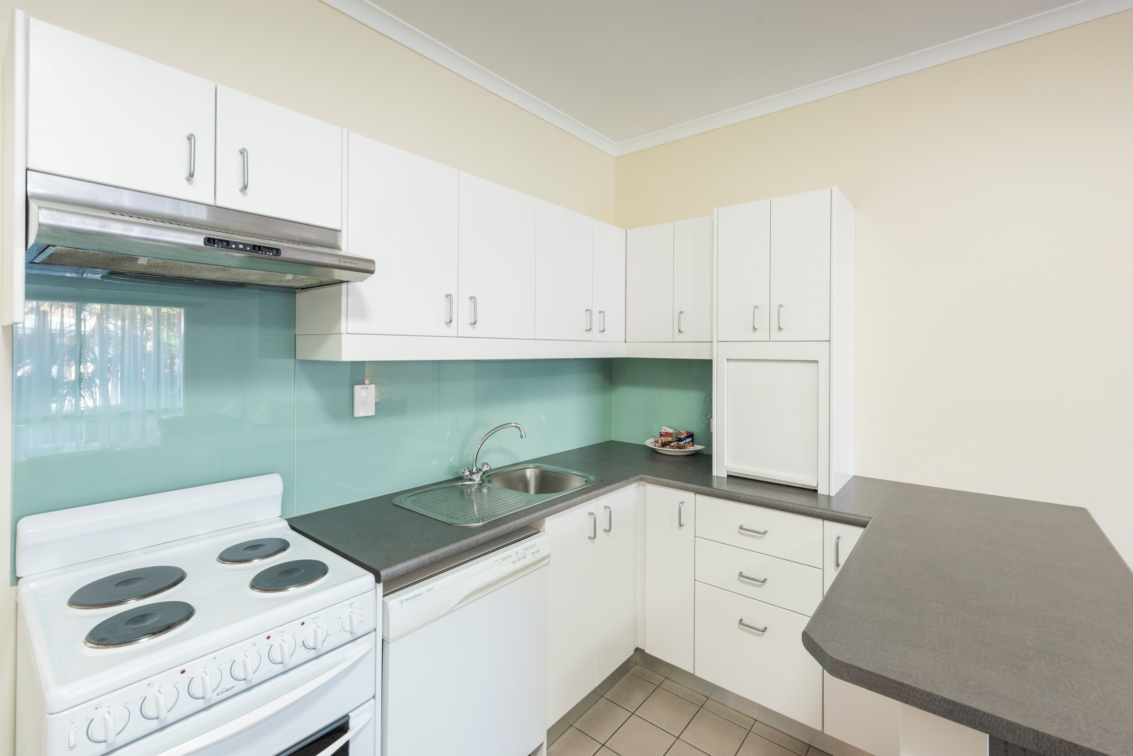 A kitchen with white cabinets, a stainless steel stove, a dishwasher, and a grey countertop.