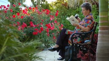 A person sitting on a bench in a garden with red flowers and greenery.