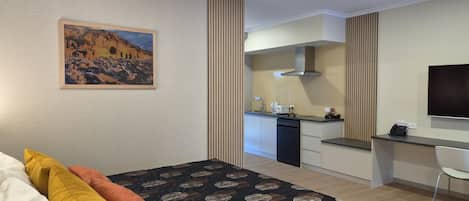 A hotel room with a bed, a painting, a kitchenette, and a TV.