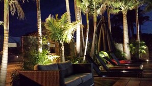 A nighttime outdoor seating area with a wicker sofa and a hammock, surrounded by palm trees and a stone wall. - McLaren Vale Motel & Apartments (McLaren Vale)