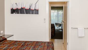 Een hotelkamer met een bed, een schilderij aan de muur en uitzicht op de eetruimte door een geopende deur.