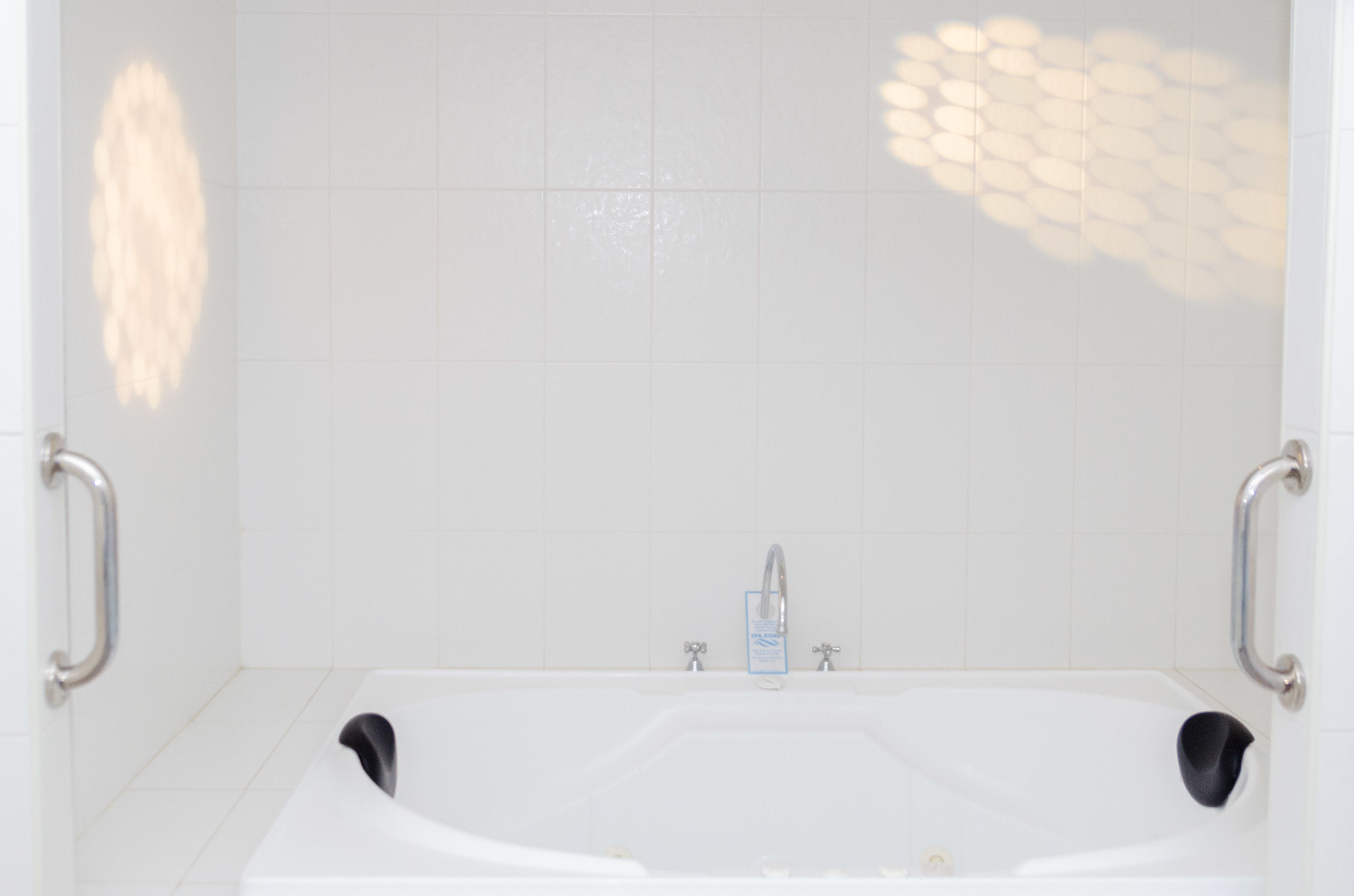 A modern bathroom with a white bathtub, chrome faucets, and a handrail on each side.