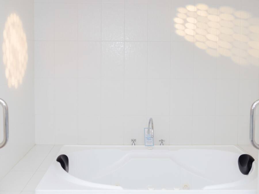 A modern bathroom with a white bathtub, chrome faucets, and a handrail on each side.