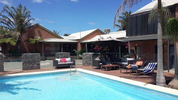A poolside area with a pool, lounge chairs, and a covered seating area with umbrellas.