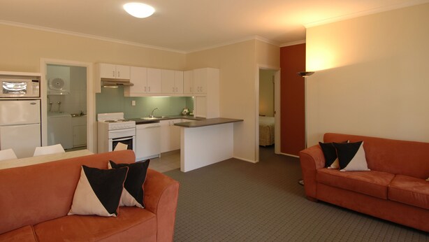 A compact living space with a kitchenette, two sofas with pillows, and a small dining area. - McLaren Vale Motel & Apartments (McLaren Vale)