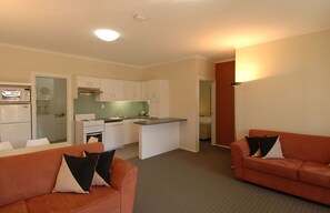 A compact living space with a kitchenette, two sofas with pillows, and a small dining area. - McLaren Vale Motel & Apartments (McLaren Vale)